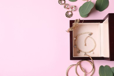 Photo of Beautiful jewelry, box and eucalyptus leaves on pink background, flat lay. Space for text
