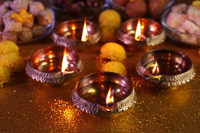 Photo of Diwali celebration. Diya lamps on shiny golden table, closeup