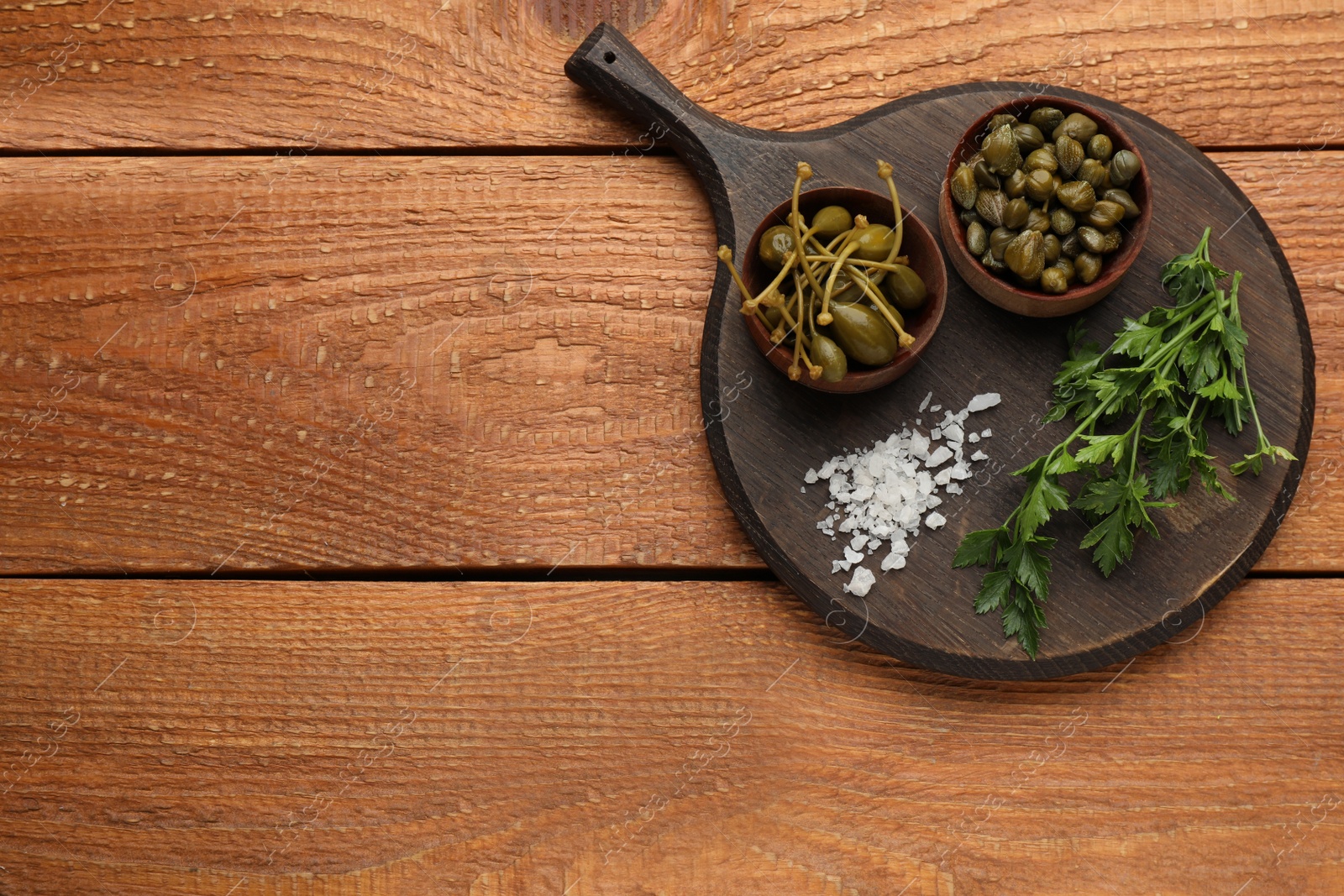 Photo of Delicious pickled capers, salt and parsley on wooden table, top view. Space for text