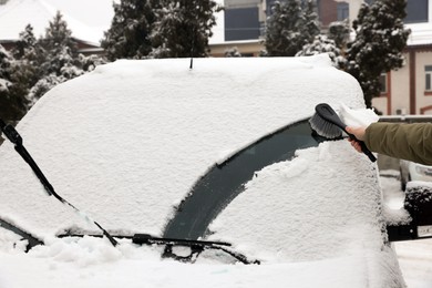 Woman cleaning car windshield from snow with brush outdoors, closeup