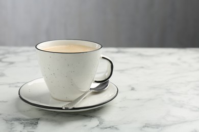 Photo of Tasty cappuccino in cup, spoon and saucer on white marble table, closeup. Space for text