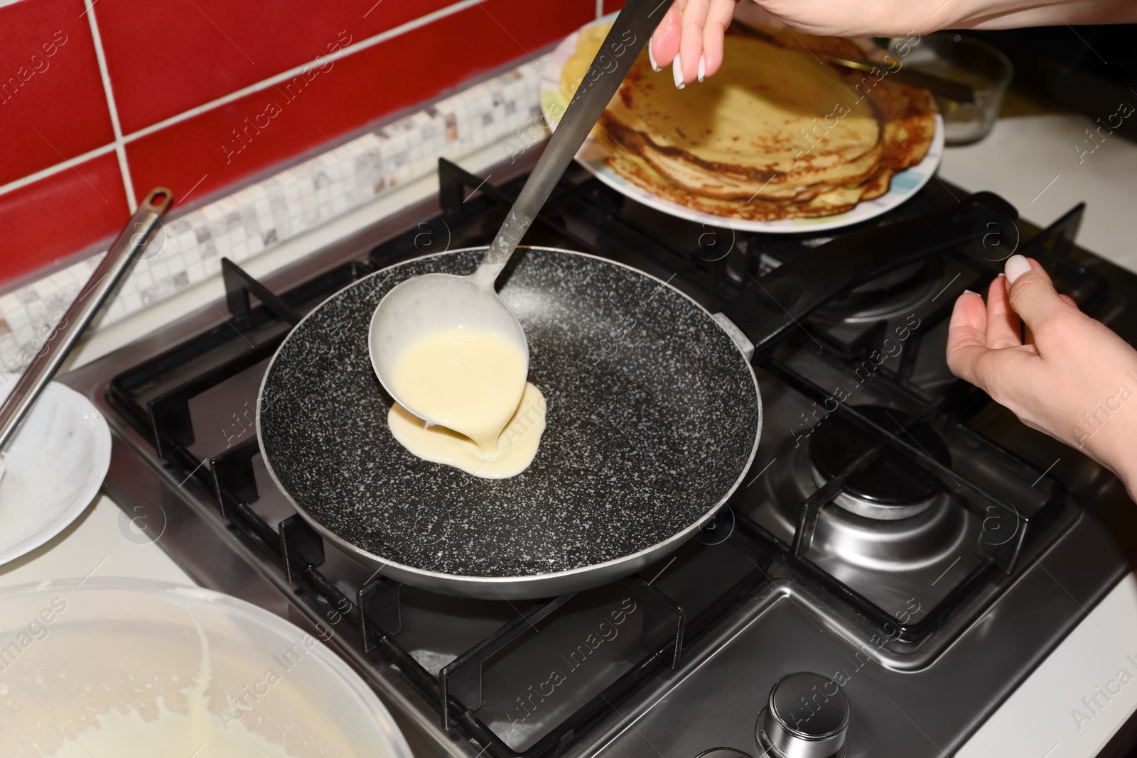 Photo of Woman pouring crepe batter onto frying pan in kitchen, closeup