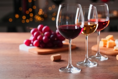 Glasses with different wines and appetizers on wooden table against blurred background. Space for text