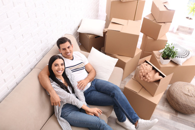 Photo of Happy couple resting in room with cardboard boxes on moving day, above view