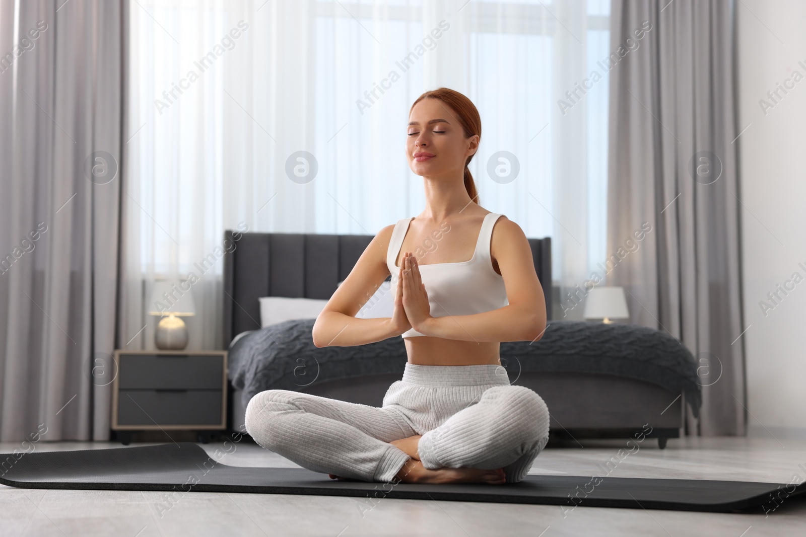 Photo of Beautiful young woman practicing Padmasana on yoga mat at home. Lotus pose