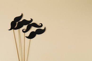 Fake paper mustaches party props on beige background, flat lay. Space for text