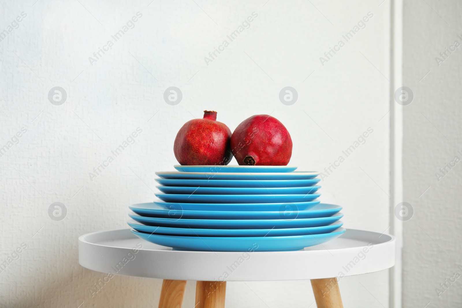 Photo of Stack of plates with pomegranates on table against light background. Interior element