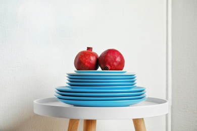 Photo of Stack of plates with pomegranates on table against light background. Interior element