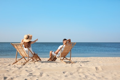 Photo of Young couple relaxing in deck chairs on beach