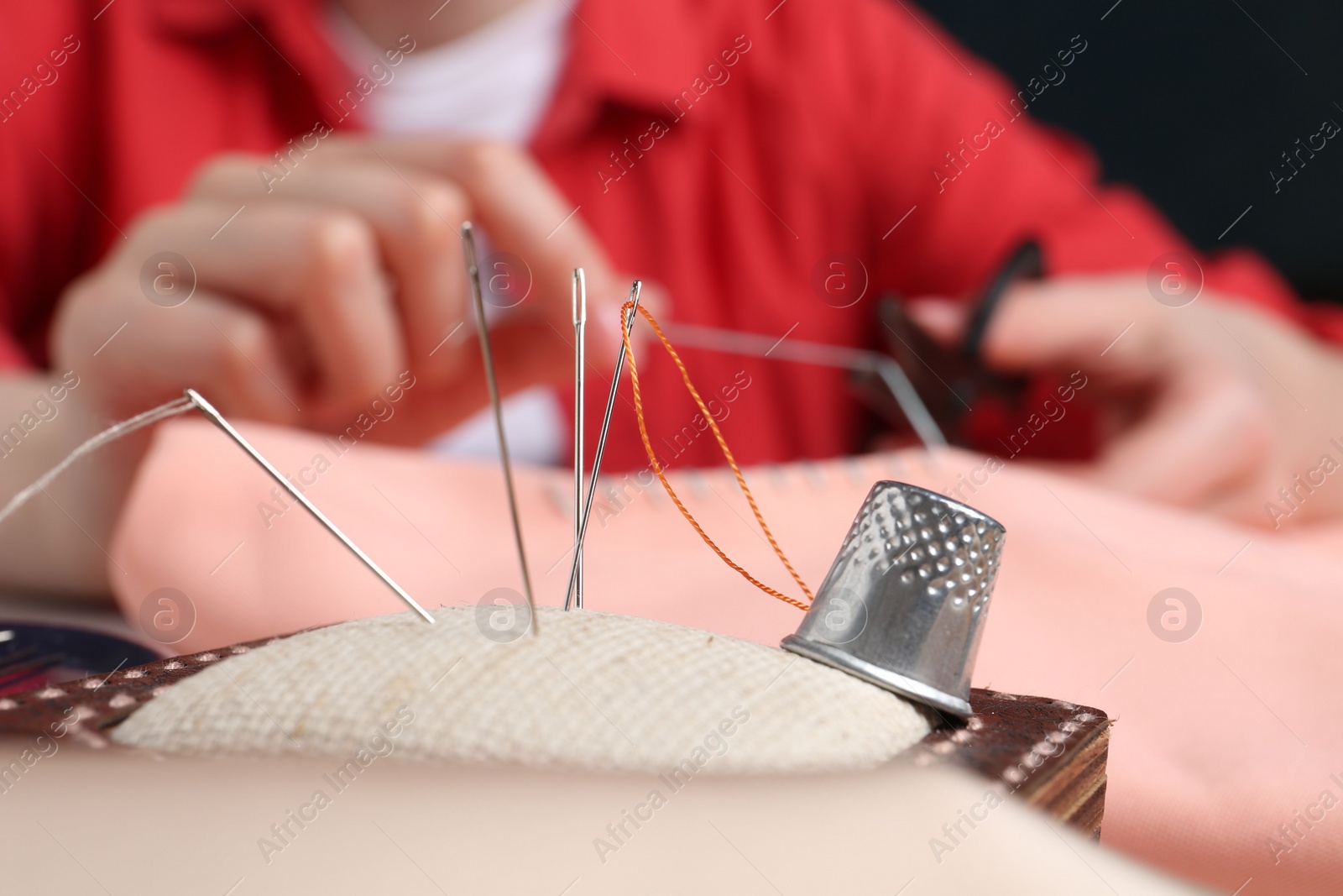 Photo of Woman cutting sewing thread over cloth, focus on pin cushion with needles and thimble