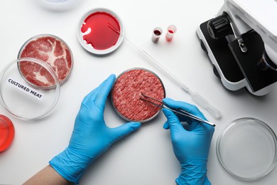 Photo of Scientist taking sample of minced cultured meat at white lab table, top view