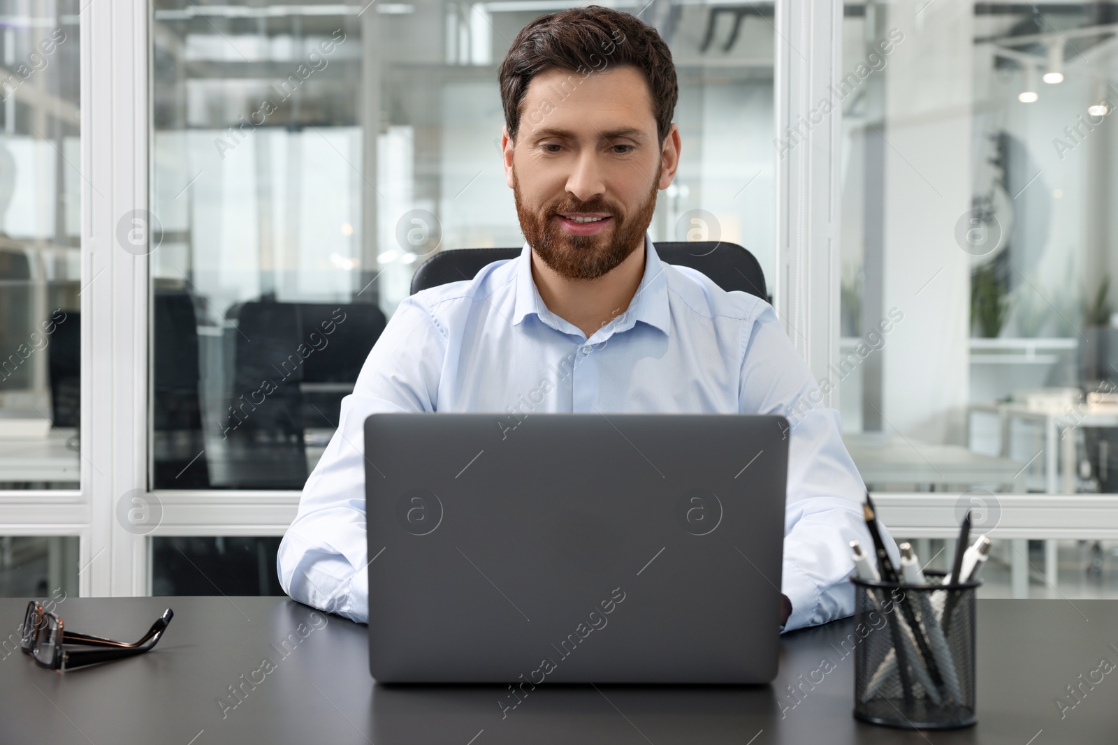 Photo of Man working on laptop at black desk in office