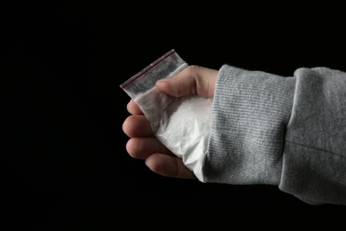 Drug dealer holding bag with cocaine on black background, closeup