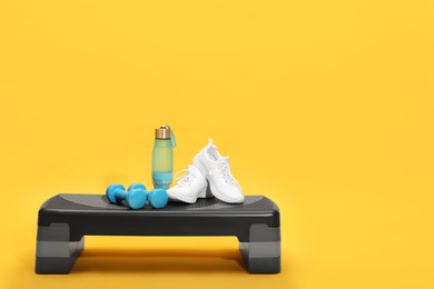 Photo of Step platform, dumbbells, shoes and bottle of water on yellow background. Sports equipment