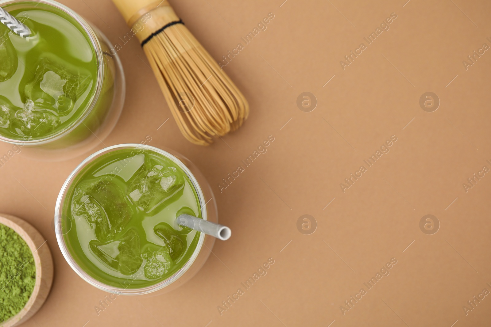 Photo of Delicious iced green matcha tea, powder and bamboo whisk on pale brown background, flat lay. Space for text