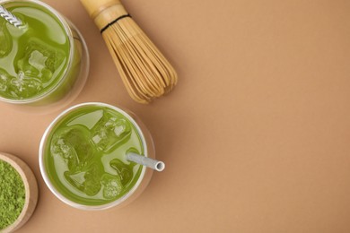 Photo of Delicious iced green matcha tea, powder and bamboo whisk on pale brown background, flat lay. Space for text