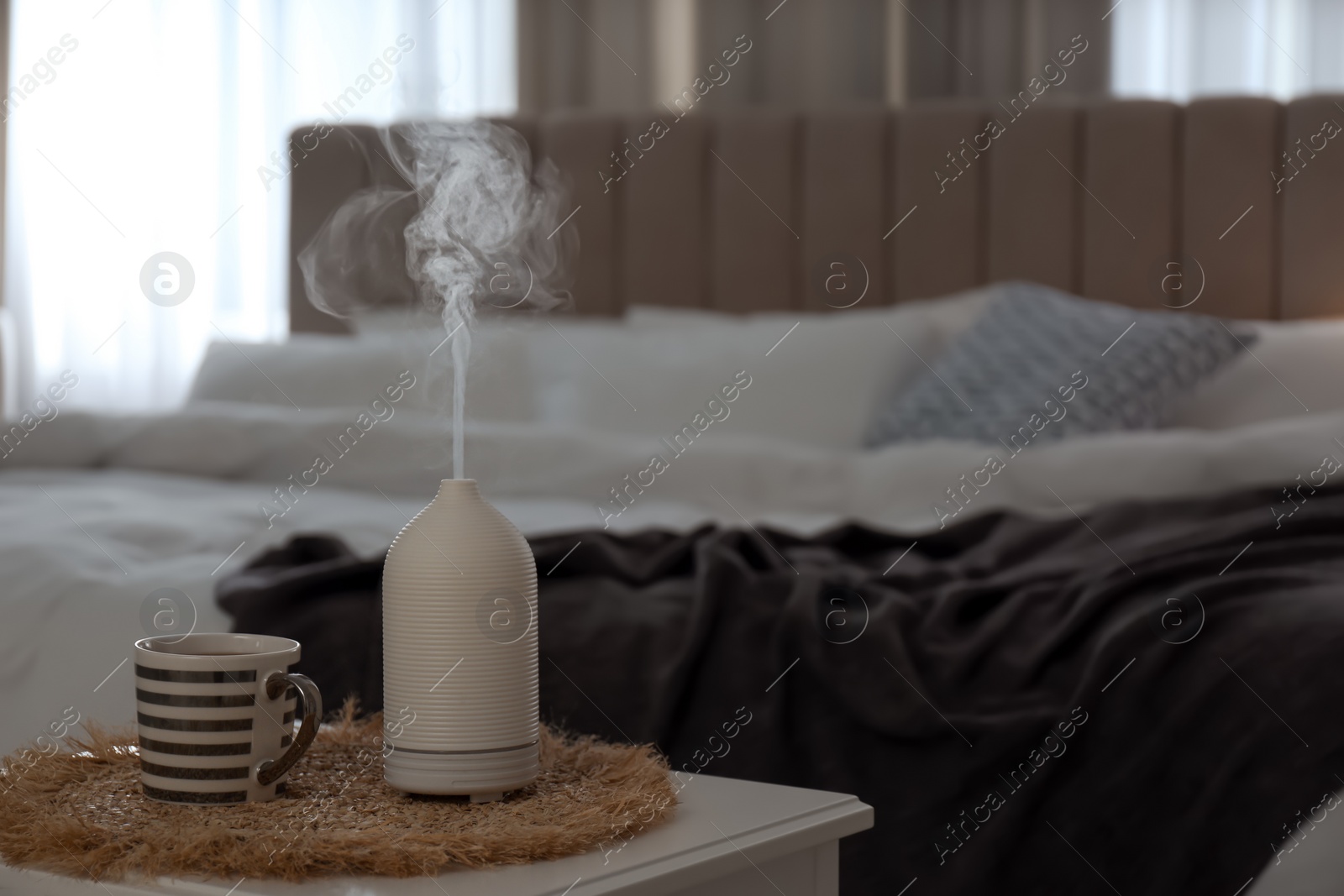 Photo of Aroma oil diffuser and cup of tea on table in bedroom. Space for text