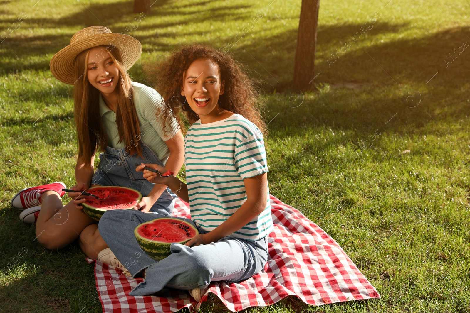 Photo of Happy girls eating watermelon on picnic blanket in park