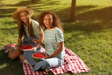 Happy girls eating watermelon on picnic blanket in park