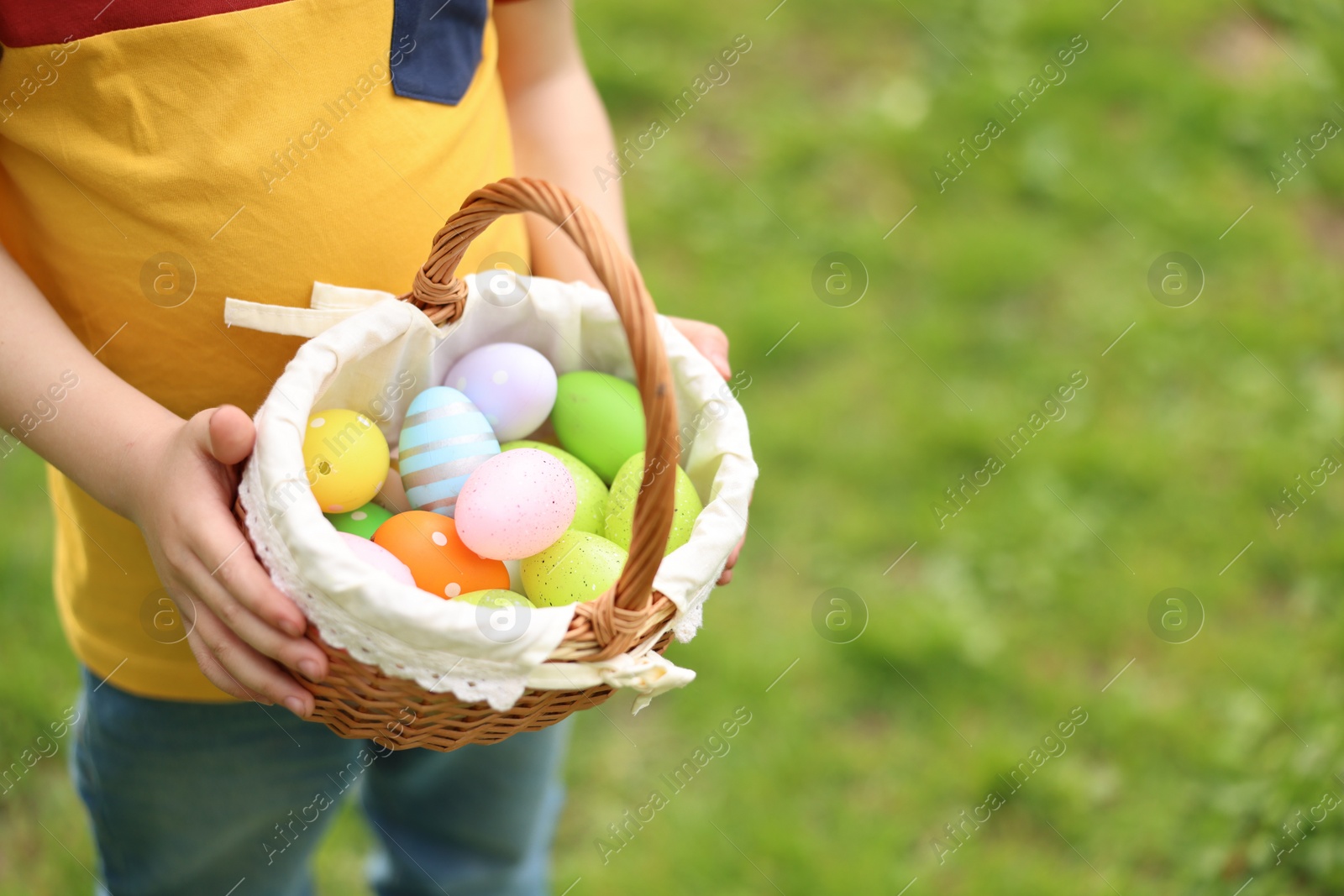 Photo of Easter celebration. Little boy holding basket with painted eggs outdoors, closeup. Space for text