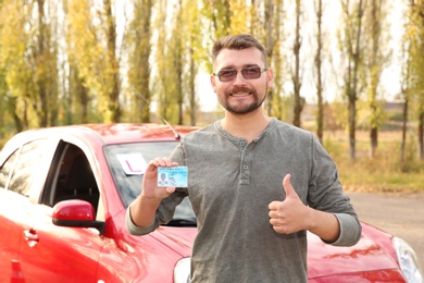 Photo of Man showing driving license near car outdoors