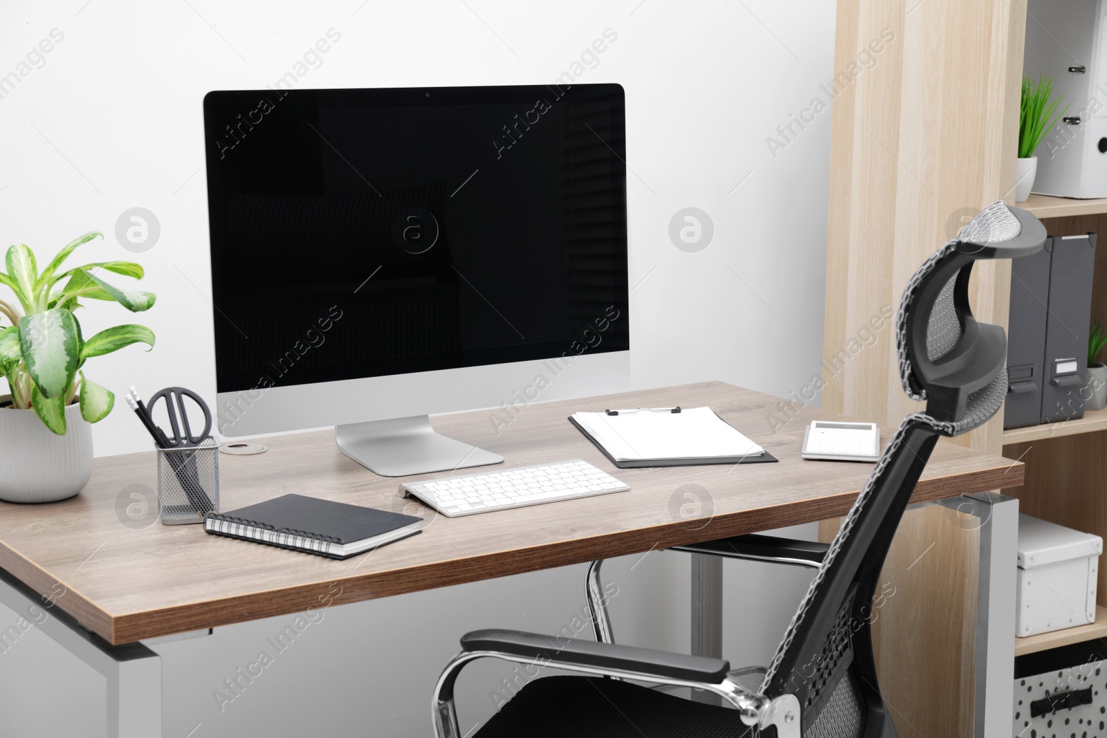 Photo of Cozy workspace with computer on desk, chair and bookcase near white wall at home