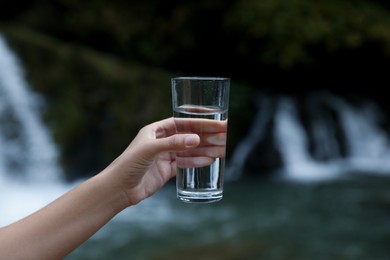 Photo of Woman holding glass of fresh water near waterfall, closeup