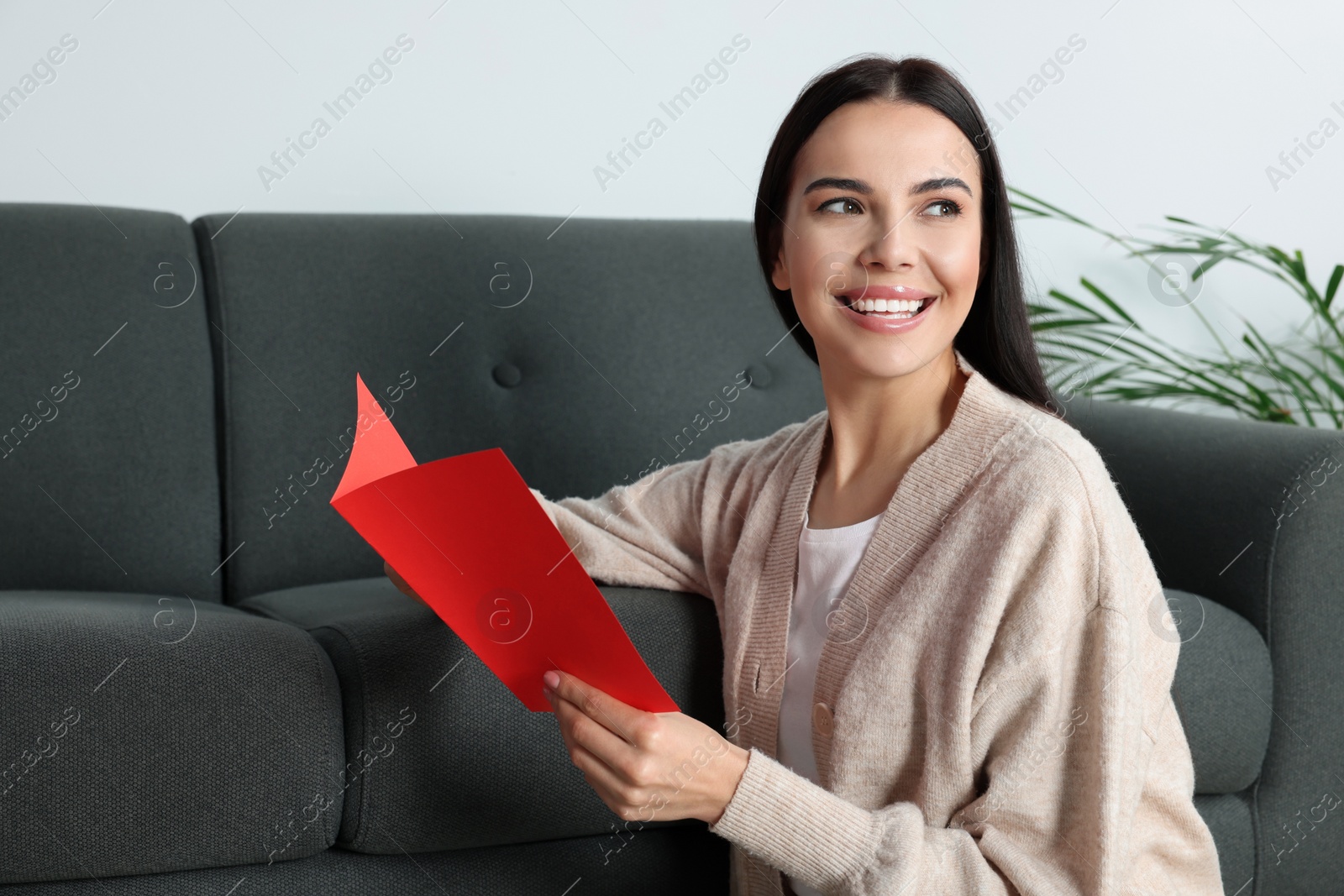 Photo of Happy woman reading greeting card on floor in living room