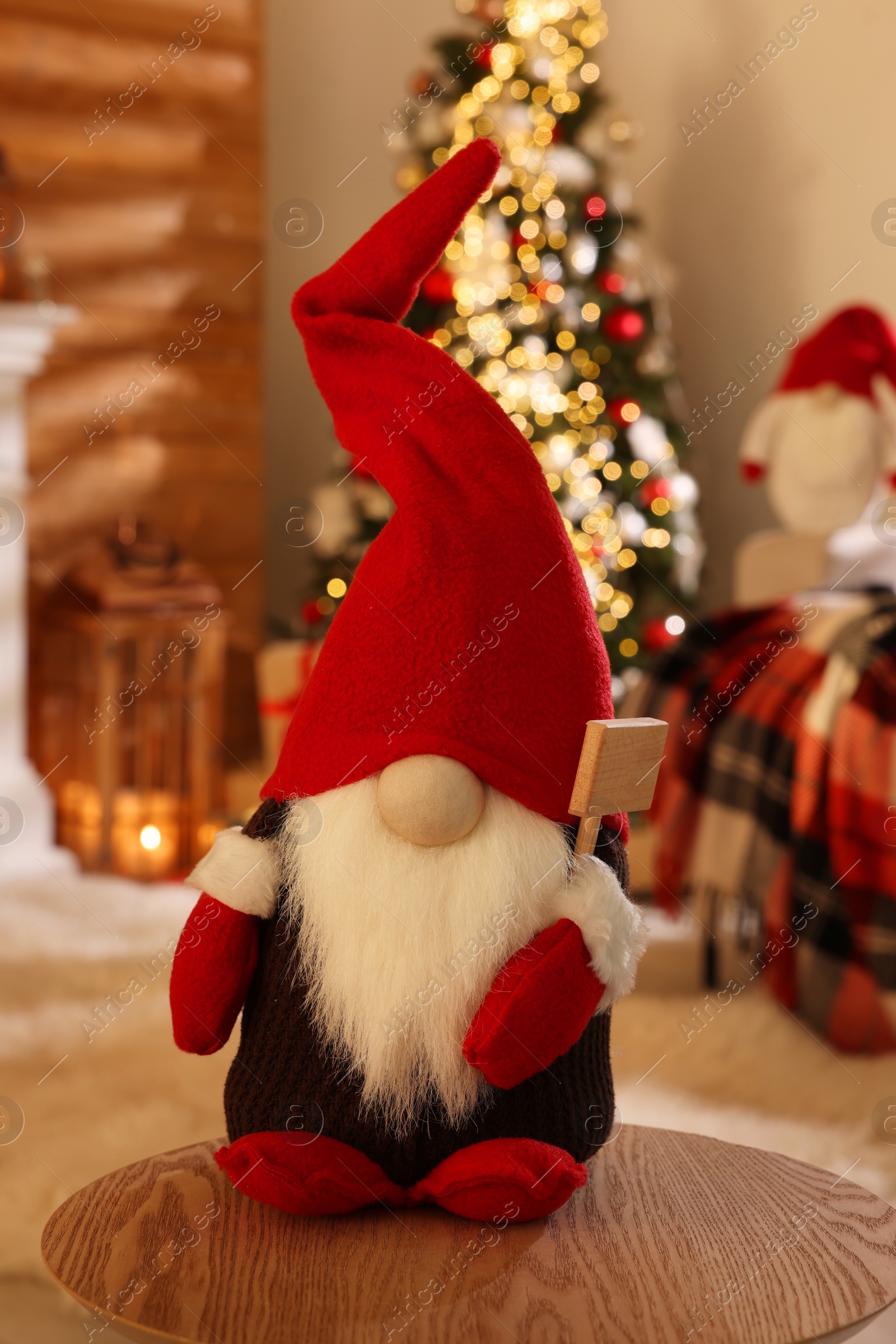 Photo of Cute Christmas gnome on wooden table in room with festive decorations