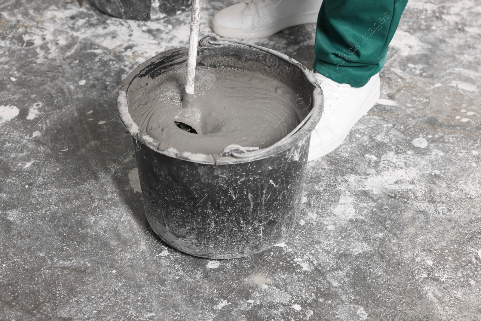 Photo of Worker mixing concrete in bucket indoors, closeup