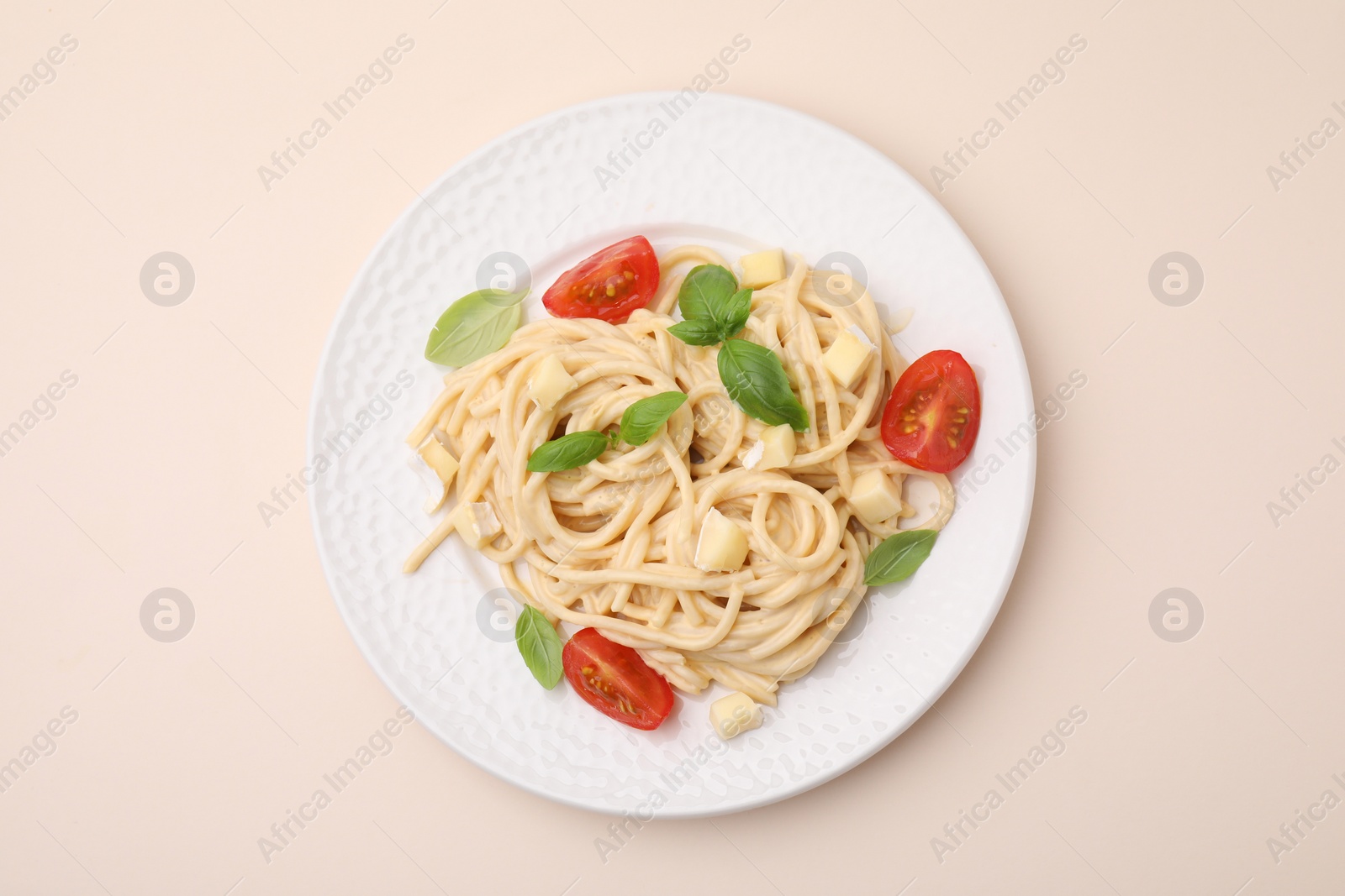 Photo of Delicious pasta with brie cheese, tomatoes and basil leaves on beige background, top view