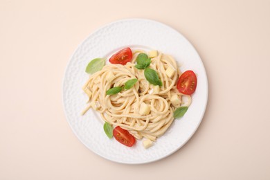 Delicious pasta with brie cheese, tomatoes and basil leaves on beige background, top view