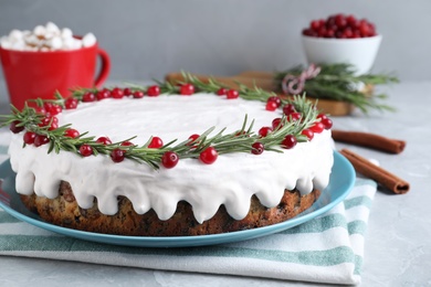 Traditional Christmas cake decorated with rosemary and cranberries on light grey marble table, closeup