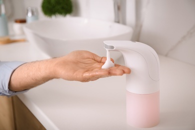 Photo of Man using automatic soap dispenser in bathroom, closeup