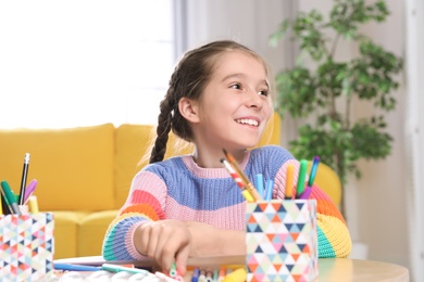 Photo of Little girl drawing picture at table with painting tools indoors