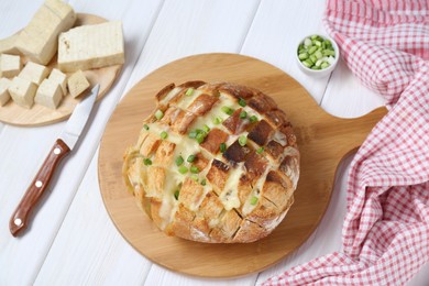 Freshly baked bread with tofu cheese, green onions and knife on white wooden table, flat lay