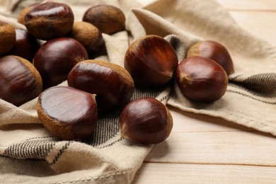 Photo of Sweet fresh edible chestnuts on light wooden table, closeup