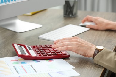 Professional accountant using calculator at wooden desk in office, closeup