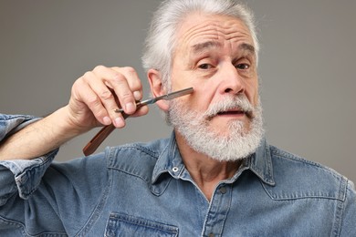 Photo of Senior man shaving beard with blade on grey background