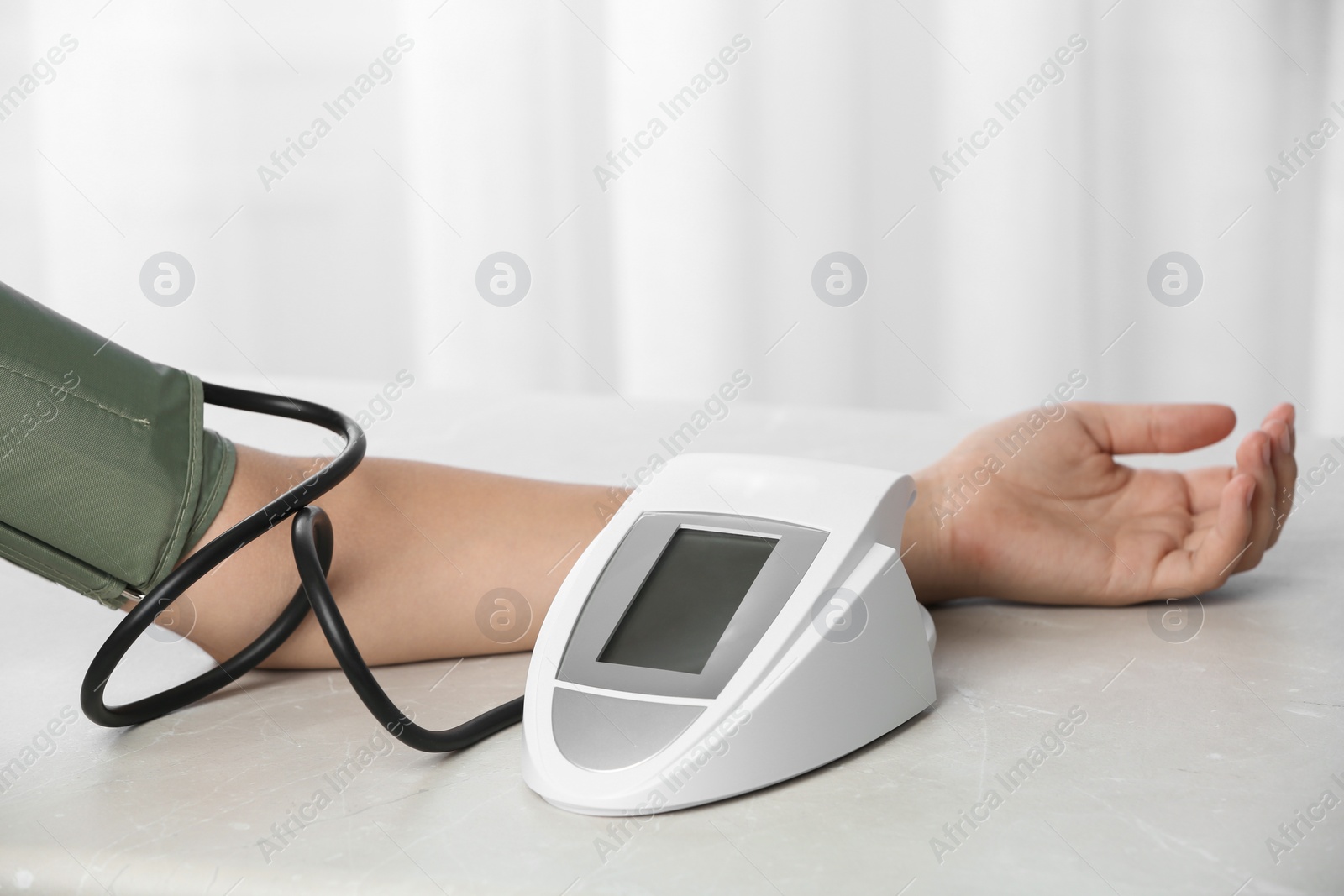 Photo of Woman checking pulse and blood pressure with sphygmomanometer on table, closeup