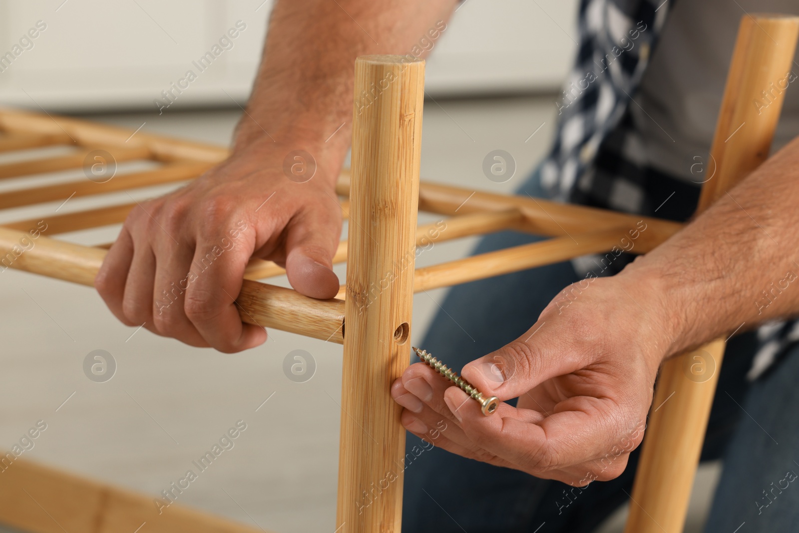 Photo of Man with self-tapping screw assembling furniture indoors, closeup