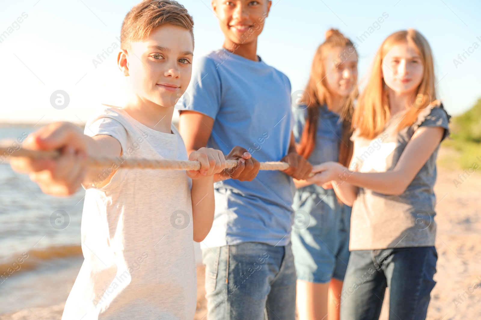 Photo of Group of children pulling rope during tug of war game on beach. Summer camp