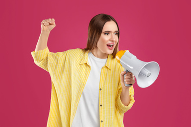 Photo of Emotional young woman with megaphone on pink background