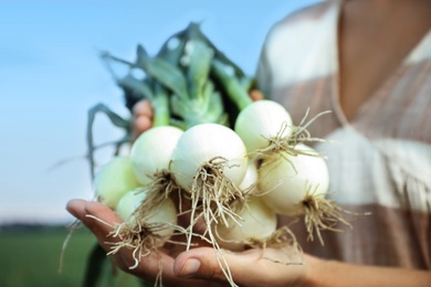 Woman holding fresh green onions outdoors, closeup