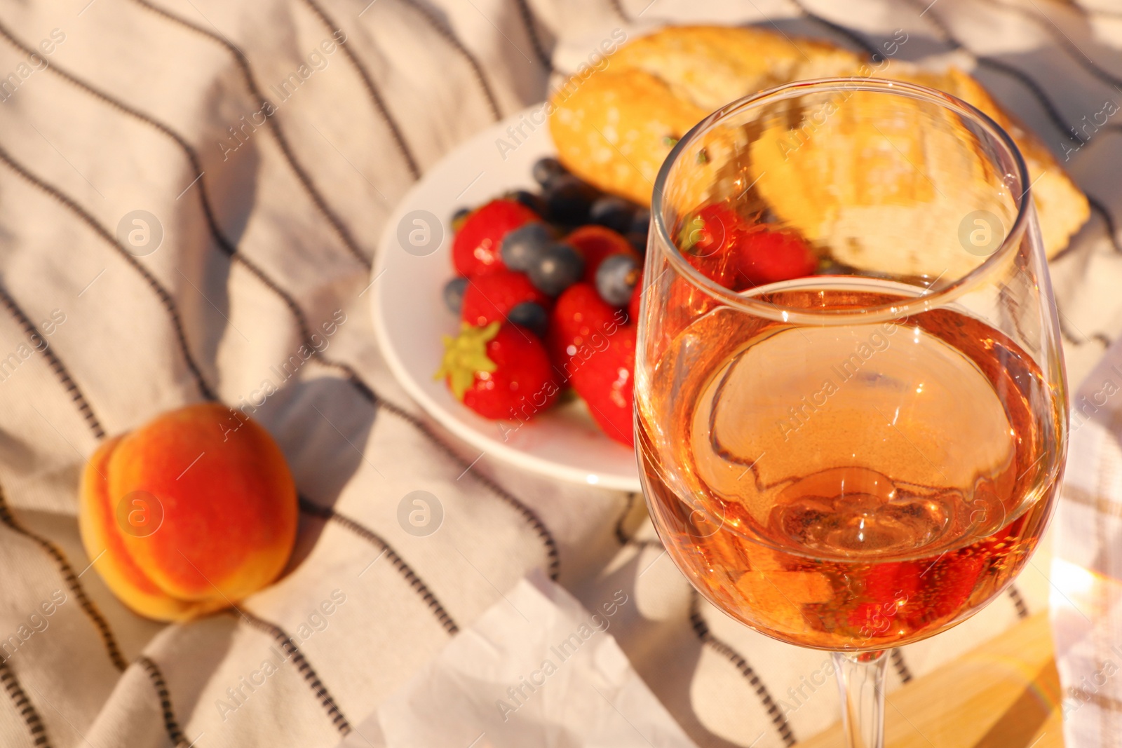 Photo of Glass of delicious rose wine and food on white picnic blanket, closeup