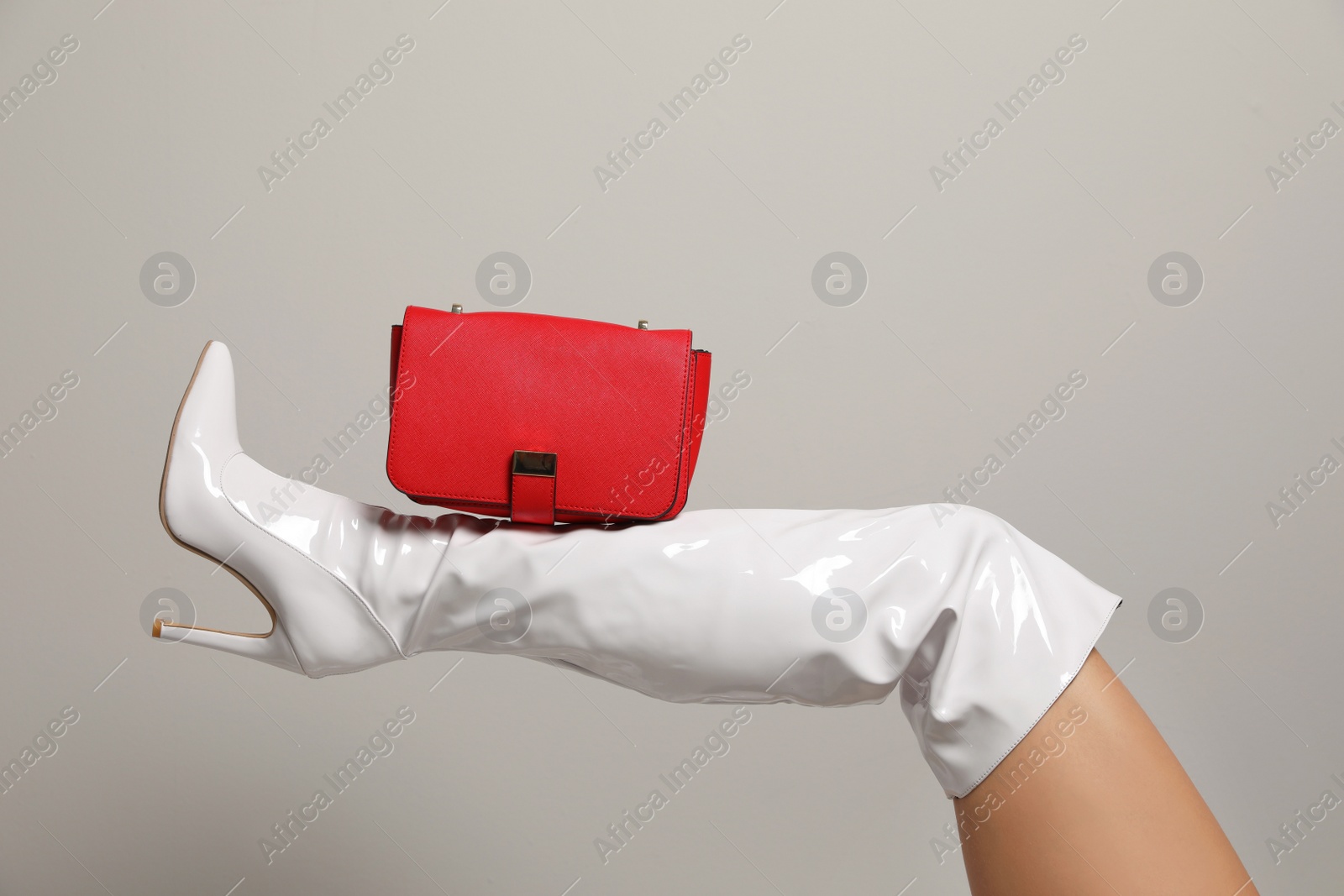 Photo of Woman wearing white long shoes with red leather bag on light background, closeup