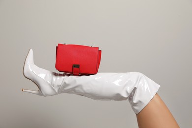 Woman wearing white long shoes with red leather bag on light background, closeup