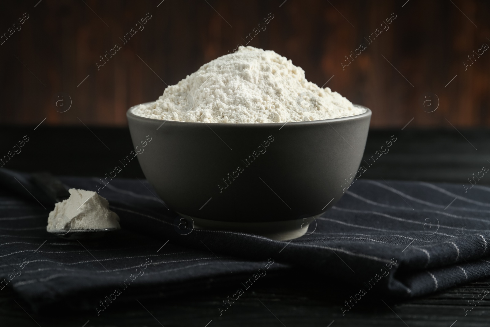 Photo of Ceramic bowl with flour on black wooden table. Cooking utensil