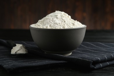 Photo of Ceramic bowl with flour on black wooden table. Cooking utensil