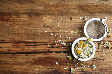 Dry chamomile flowers in infuser on wooden table, flat lay. Space for text